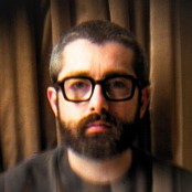 Man with glasses posing infront of curtain